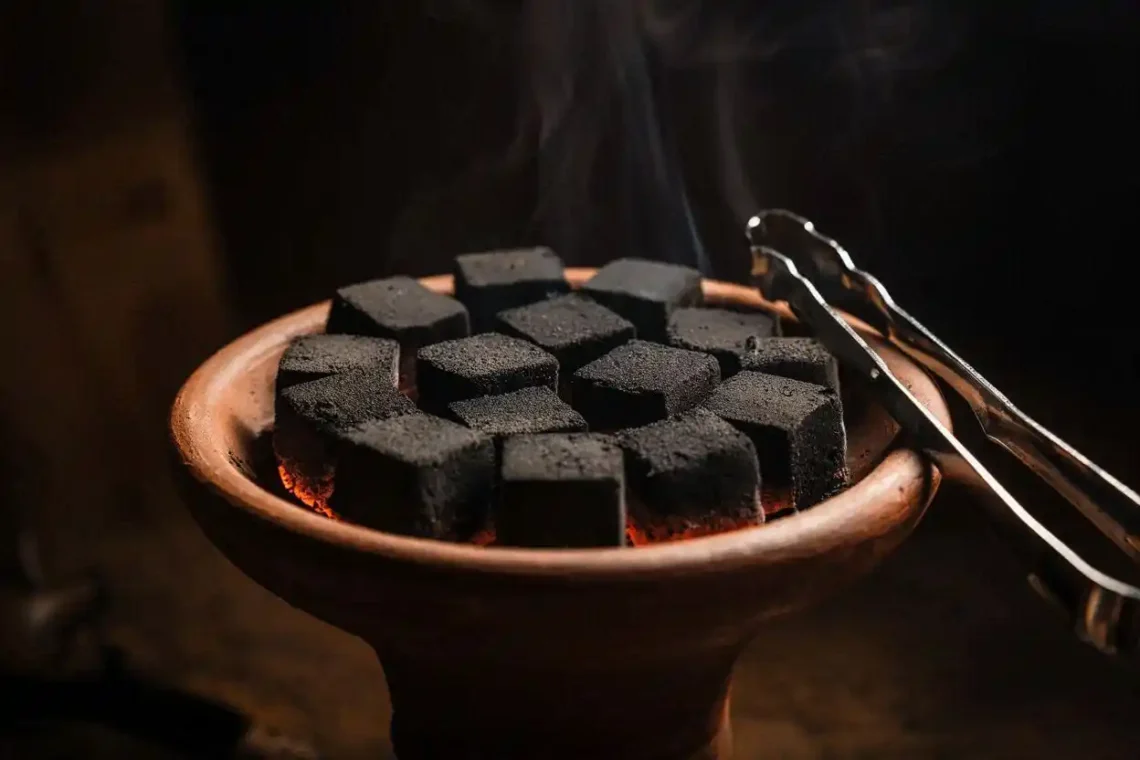 Natural coconut charcoal briquettes for hookah arranged on a clay bowl with tongs nearby